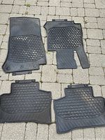 Photo of four black rubber floor mats for a Mercedes GLC 2020 and newer models, showing front and rear mats laid out on a stone patio surface. Mats are lightly used and need cleaning.
