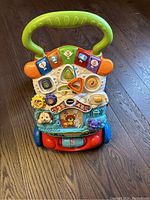 Photo of a colorful VTech baby activity walker toy with interactive buttons, animal figures, and spinning gears on a wood floor.