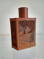 Front side of bamboo tea caddy showing carved figure on boat among reeds and Chinese characters on side panels.