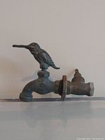 Side view of the brass garden hose spigot showing the hummingbird handle and mounting flange in profile.