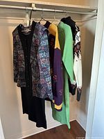 Five vintage clothing pieces hanging on a rod, including sweaters and a black dress with a patterned cardigan.