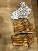 Top view of a bundle of white plastic hangers and two bundles of natural wood hangers with metal hooks on a wooden floor.