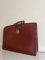 Three quarter view of the brown leather briefcase showing metal clasp, handle and side compartments.