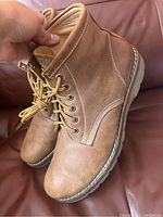 Pair of men's Roots Tribe leather boots shown from front-side angle, held up by hand to display condition and details.