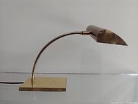 Side view of vintage brass desk lamp with rectangular base and curved gooseneck arm with tapered lamp shade.