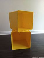 Two yellow acrylic storage cubes stacked, showing side view with ventilation holes and minor surface marks.