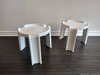 Two white plastic side tables shown side by side on floor against wall