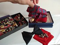 Photo showing red and blue paisley patterned suspenders in a box alongside black bow tie, red pocket square, and silver-tone cuff links