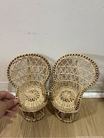 Front view of two vintage mini peacock rattan chairs placed side by side against a wall, showing detailed weaving and circular seats.