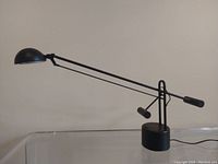 Full profile view of black adjustable desk lamp on clear surface