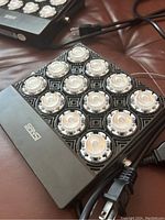 Close-up of one Sansi LED grow light showing 12 LED bulbs arranged in a 3x4 grid with ceramic insulation and power cord.