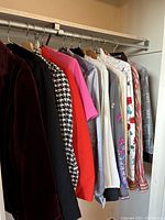 Side view of vintage women's clothing hung on metal rod showing variety of colors, patterns and fabrics including floral embroidery and houndstooth pattern.