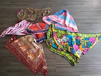 Photo showing the collection of six vintage scarves laid out on a gray wood floor; various colors and patterns visible including floral, paisley, stripes, and abstract.
