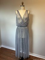 Front view of a women's formal sleeveless dress in light gray with a V-neck and beaded waistband on a dress form.