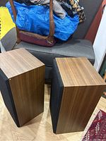 Pair of two Yamaha speakers with wooden sides and black fabric on the front, positioned upright on a wood floor with background furniture.