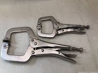 Photo showing two woodworking vice grip clamps, one smaller approximately 6 inches and one larger approximately 9 inches, both made of metal with adjustable screws and locking handles.