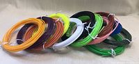 12 rolls of 3D pen printer filament refills in multiple colors, each tied with white bands, arranged in rows.