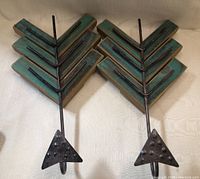 Two arrow-shaped wall hooks made from wood and metal. Wood is painted in distressed green with black metal detailing. Hooks extend downward from the metal arrow tips with rivet accents.