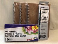 Photo showing three spiral bound sketch books with brown kraft paper covers, Pentel Arts 16 color oil pastel set and Kasimir 14 drawing pencils package.
