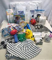 Overview of baby feeding bottles, pacifiers, toys including rubber ducks, and gray plush elephant lovey with other baby items on a white surface.