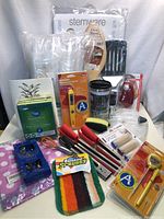 Photo showing multiple kitchenware and houseware items including boxed stemware oven shelf, plastic glasses, red handled knives, whisk, cleaning sponges, and thermometer packaging.