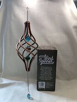 Photo showing kinetic wind spinner with copper-colored frame and blue, green orbs next to product box.