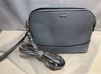 Front view of the grey Lovevook purse with attached strap and an additional long strap wrapped in plastic beside it.