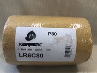 Close-up of sealed roll of sanding discs in plastic wrap with label showing brand, quantity and grit size.