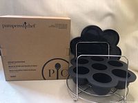 Pampered Chef Silicone Egg Bite Mould in box alongside the silicone mould and metal carrier stand.