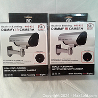 Front view of the two boxed dummy IR security cameras showing brand, model number, and features including flashing red light, suitable for indoor/outdoor use.