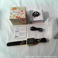 Kids GPS watch phone with black silicone wrist strap featuring yellow paw prints, USB charging cable, additional wrist strap, instruction manual, and box.