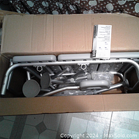 Opened cardboard box showing disassembled parts of a gray Medline transfer bench, including armrests and metal frame.