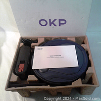 Robot vacuum cleaner in blue, placed in protective packaging alongside charging dock and user manual, all inside original box with OKP branding.