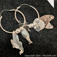 Pair of sterling silver hoop earrings on black background, each with an animal charm, a fish charm, and a bead.