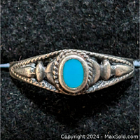 Front view of sterling silver ring with center oval turquoise stone and detailed silverwork around it.