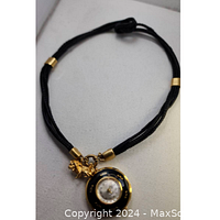 Full view of necklace showing black multi-strand cord and round enamel watch pendant with gold accents and a small lion charm near the clasp.