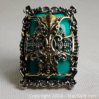 Front view showing large turquoise stone with gold and silver tone filigree detailing.
