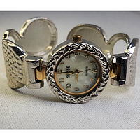 Close-up photo of the watch front face showing white dial, gold-tone numerals and hands, and textured silver band with gold accents.