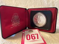 Coin displayed in open red velvet-lined case with Calgary coat of arms and centennial dates