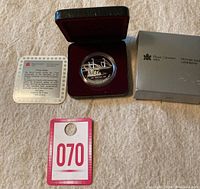 The coin displayed in its original red velvet-lined case alongside its certificate and outer box.