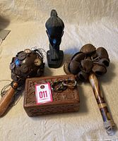 Photo of ethnic decorative items including carved wooden head, wooden rattles with seed pods and coins, and a carved wooden box with beads on top.