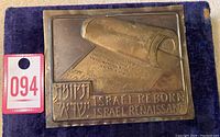 Photo showing embossed copper plaque with Hebrew scroll and inscriptions 'Israel Reborn Israel Renaissance' and a lot number tag (094)