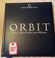 Dark blue leatherbound cover of the book 'Orbit' by National Geographic Society with authors Jay Apt, Michael Helfert, and Justin Wilkinson.