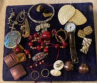 A full view of all jewelry items inside the lot arranged on a dark blue background showing diverse vintage pieces including rings, earrings, bracelets, a necklace, brooch and wristwatch.