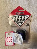 View of the front of the Wham-O Hacky Sack Kicker footbag still sealed inside original plastic packaging with red and white cardboard backing.