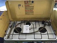 Top view showing open lid, three burners with grates, propane hose, and spark igniter.