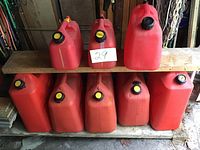Photo showing 3 cans on top shelf and 5 cans on bottom shelf arranged on wooden shelves in garage setting.
