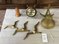 Top view of all items: brass ship's bell, barometer designed as ship's wheel with brass spokes and wood frame, three brass seagulls (large, medium, small), and brass/copper brush case