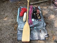Overview photo of all boating accessories including three ropes, one bumper, one paddle, sunglasses, motor flusher and keychain on tarp outdoors.