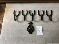 Five black metal hooks including four horseshoe-shaped hooks and one decorative hook shown side by side on a white surface